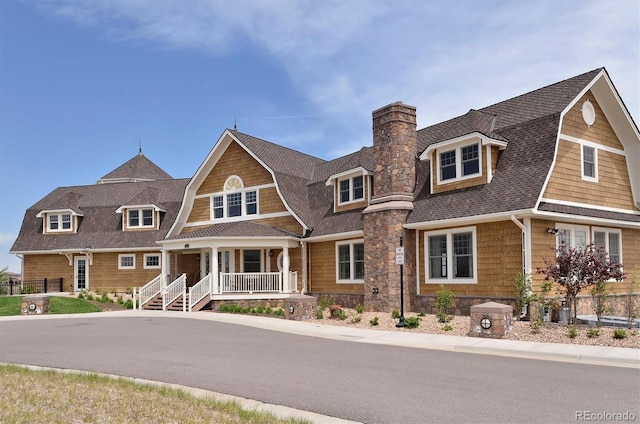 shingle-style home featuring roof with shingles, covered porch, a chimney, and a gambrel roof