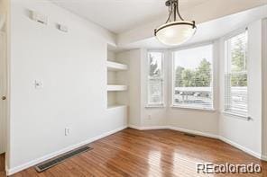 unfurnished dining area with built in shelves and hardwood / wood-style floors