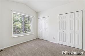 unfurnished bedroom with carpet, lofted ceiling, and two closets