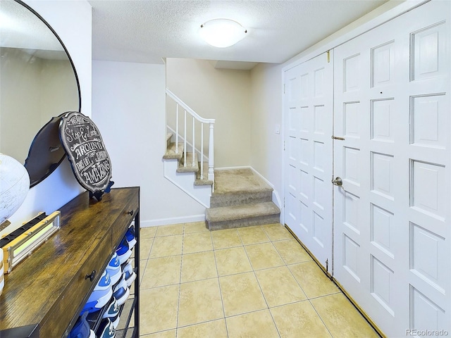 entrance foyer featuring a textured ceiling, stairs, light tile patterned flooring, and baseboards