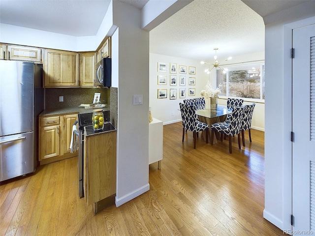 kitchen featuring appliances with stainless steel finishes, dark countertops, a chandelier, and light wood finished floors
