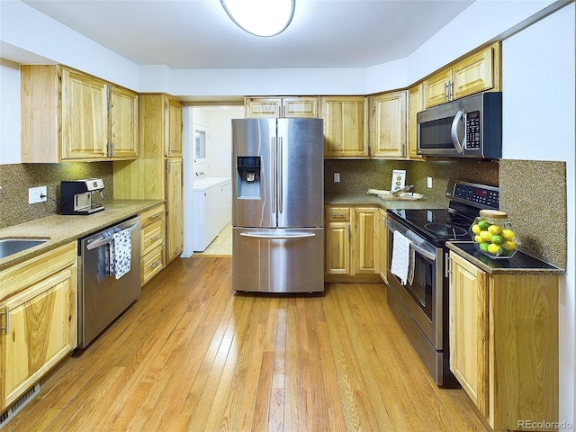 kitchen featuring appliances with stainless steel finishes, light wood-type flooring, decorative backsplash, and separate washer and dryer