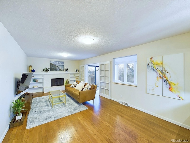 living room with a textured ceiling, baseboards, wood finished floors, and a glass covered fireplace