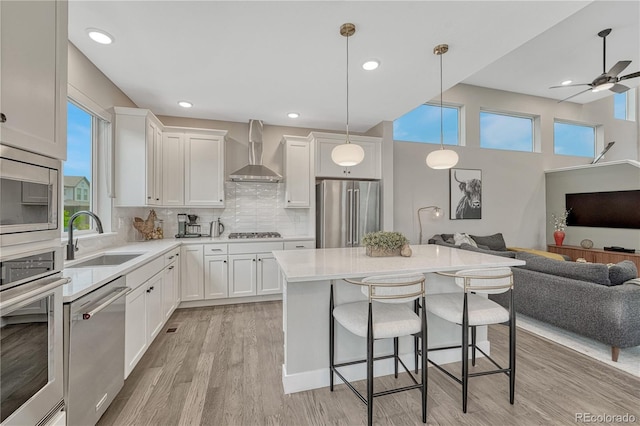 6366 N Emporia St, Denver, CO 80238 - kitchen with stainless steel appliances, wall chimney exhaust hood, open floor plan, a breakfast bar area, and light wood-style flooring