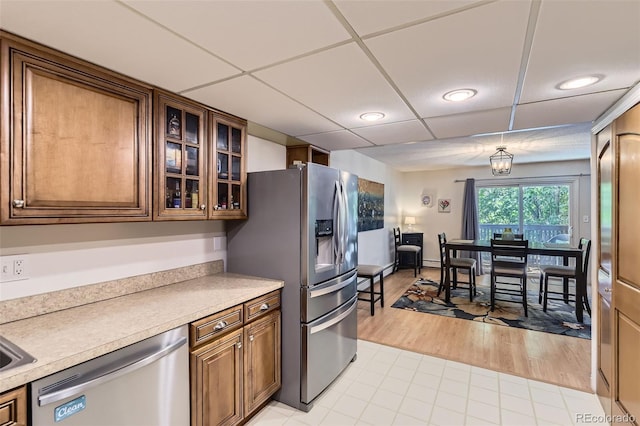 7020 E Girard Ave Unit 206, Denver, CO 80224 - kitchen featuring appliances with stainless steel finishes, light countertops, a drop ceiling, brown cabinets, and glass insert cabinets
