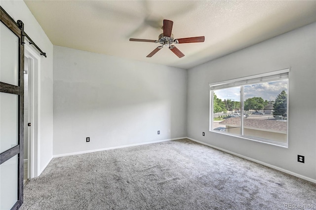 empty room with ceiling fan, a barn door, and carpet floors