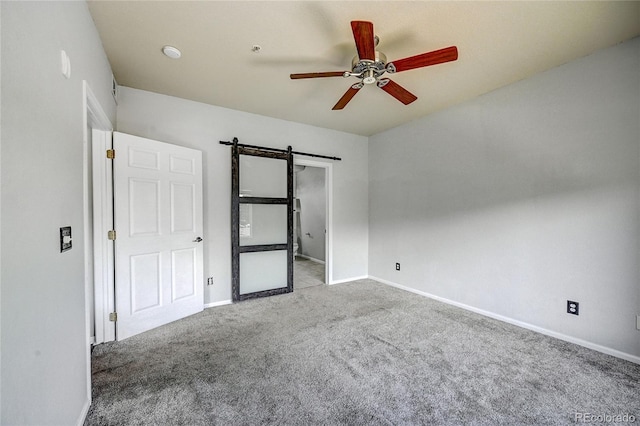 unfurnished bedroom with light carpet, a barn door, and ceiling fan