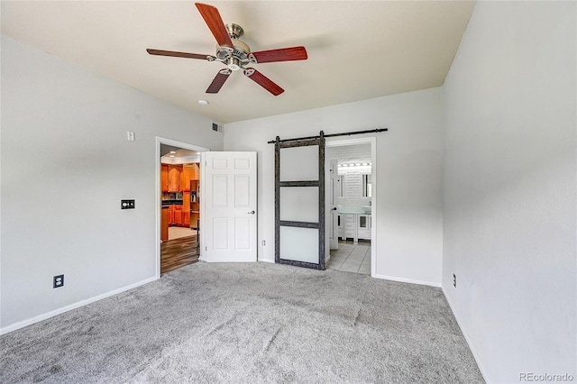 unfurnished bedroom featuring stainless steel refrigerator with ice dispenser, ensuite bathroom, light colored carpet, ceiling fan, and a barn door