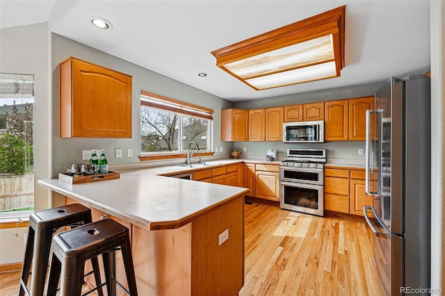 9515 Dolton Way, Highlands Ranch, CO 80126 - kitchen featuring appliances with stainless steel finishes, a peninsula, a sink, light wood-style flooring, and a kitchen bar
