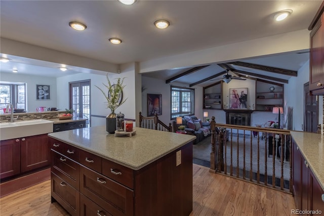 kitchen featuring light stone countertops, light wood-type flooring, ceiling fan, vaulted ceiling with beams, and sink