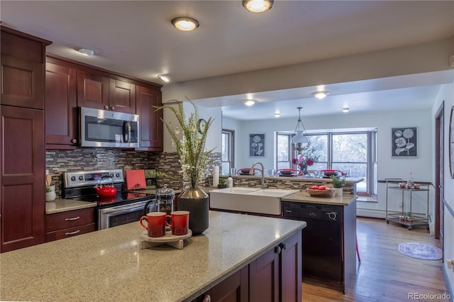 kitchen featuring stainless steel appliances, light stone countertops, sink, decorative light fixtures, and backsplash