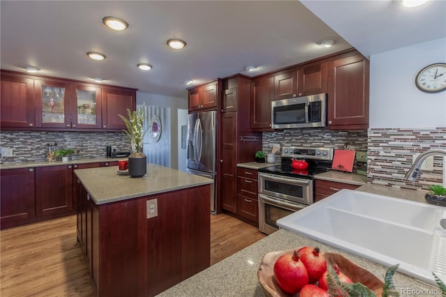 kitchen featuring appliances with stainless steel finishes, a center island, light stone counters, sink, and light hardwood / wood-style flooring