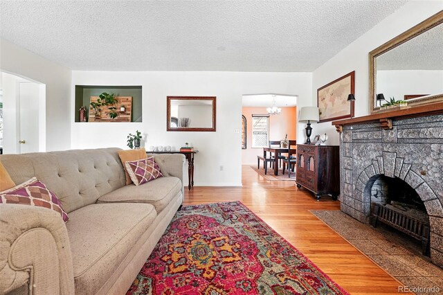 1332 Ash St, Denver, CO 80220 - living area with light wood-style floors, a chandelier, a textured ceiling, arched walkways, and a fireplace