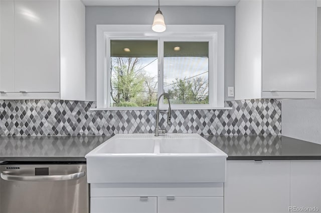 kitchen featuring stainless steel dishwasher, a sink, white cabinets, dark countertops, and decorative light fixtures