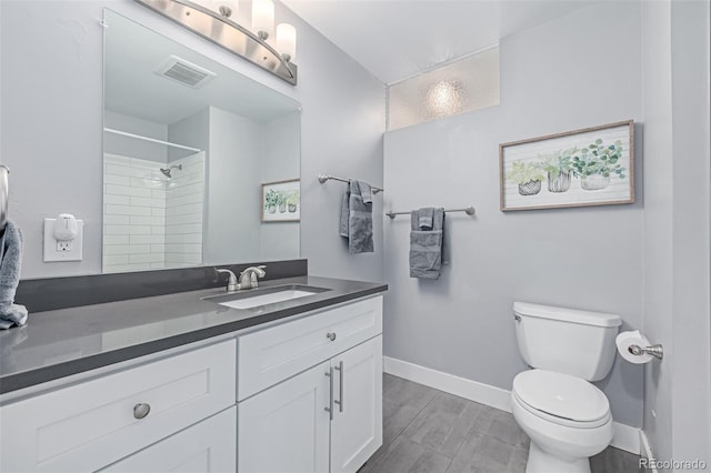 bathroom with toilet, baseboards, a tile shower, and vanity