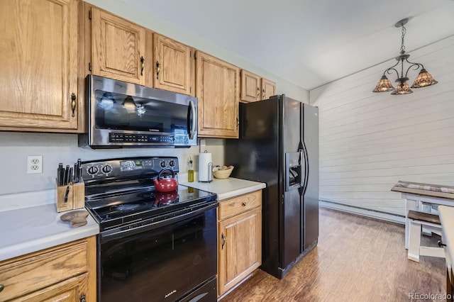 kitchen featuring pendant lighting, light countertops, wood walls, wood finished floors, and black appliances