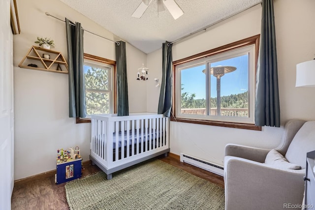 bedroom with a textured ceiling, multiple windows, baseboard heating, and wood finished floors