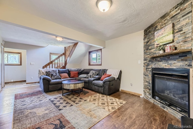 living area featuring a fireplace, stairway, a textured ceiling, wood finished floors, and baseboards