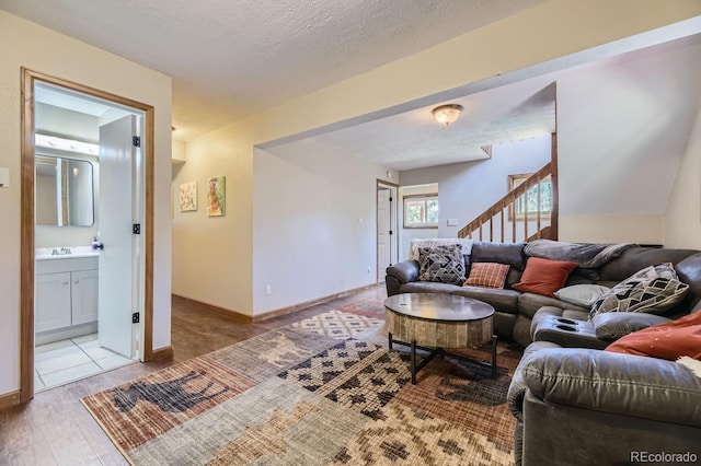 living room with stairway, baseboards, a textured ceiling, and wood finished floors