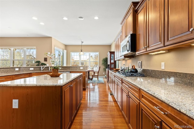 kitchen with appliances with stainless steel finishes, a healthy amount of sunlight, a kitchen island, and light hardwood / wood-style flooring