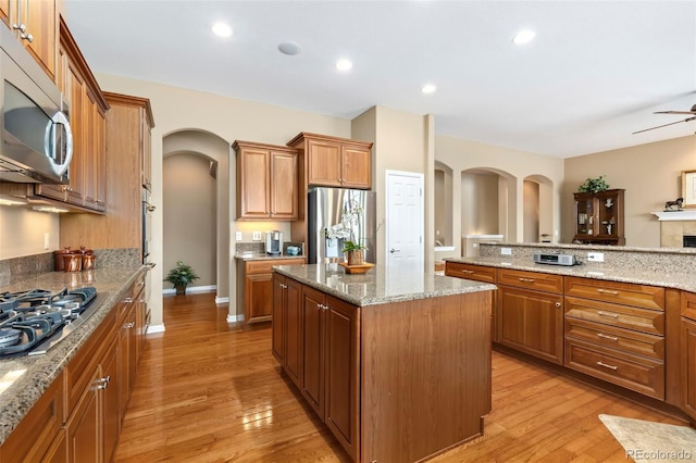 kitchen featuring light wood-type flooring, light stone countertops, a kitchen island, and appliances with stainless steel finishes