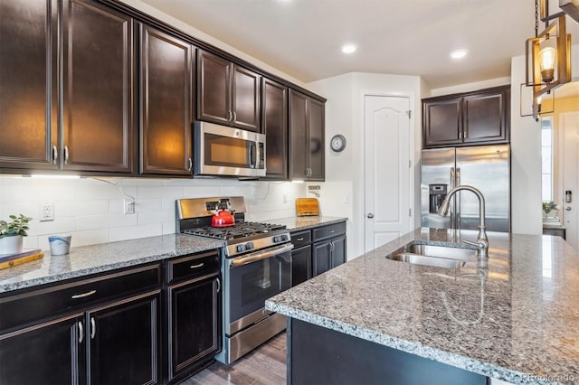 kitchen featuring stainless steel appliances, light stone countertops, sink, and a center island with sink