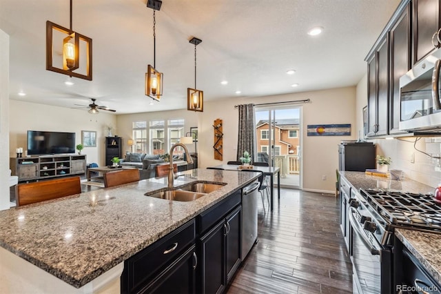 kitchen featuring pendant lighting, sink, backsplash, stainless steel appliances, and a center island with sink