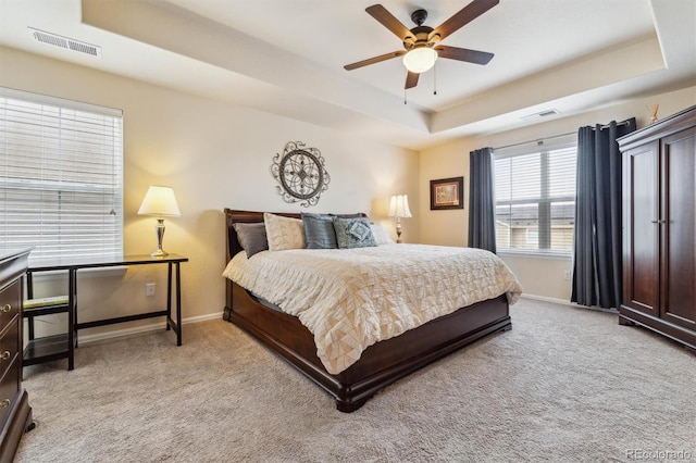 carpeted bedroom with ceiling fan and a tray ceiling