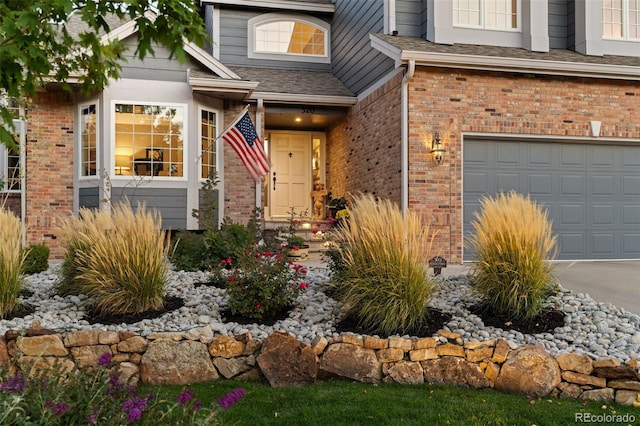 entrance to property featuring a garage, brick siding, and a shingled roof