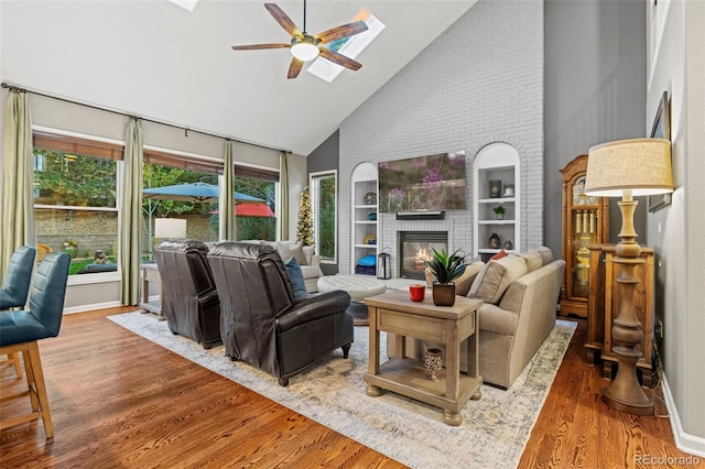 living area with baseboards, a ceiling fan, wood finished floors, a brick fireplace, and high vaulted ceiling