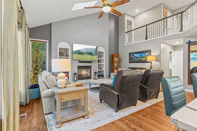 living area with high vaulted ceiling, a fireplace, wood finished floors, and a ceiling fan