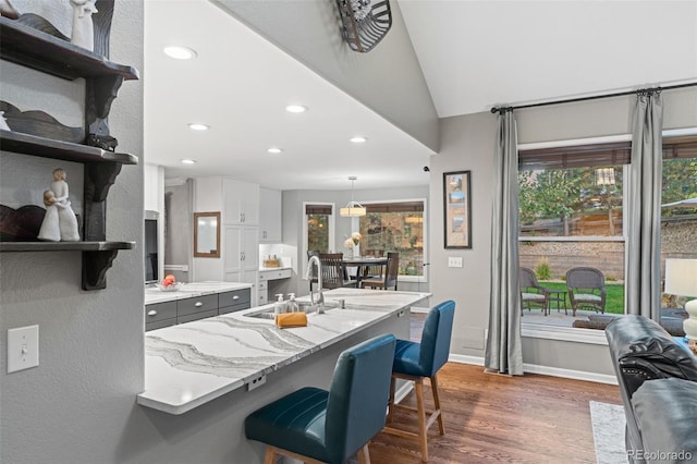 kitchen with a breakfast bar area, open shelves, dark wood-type flooring, white cabinetry, and a sink