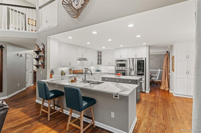 kitchen featuring wood finished floors, a peninsula, stainless steel appliances, under cabinet range hood, and a sink