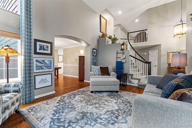 living area featuring arched walkways, high vaulted ceiling, dark wood-type flooring, a healthy amount of sunlight, and stairway