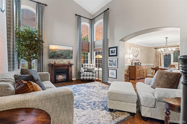 living area featuring arched walkways, a glass covered fireplace, wood finished floors, high vaulted ceiling, and a chandelier