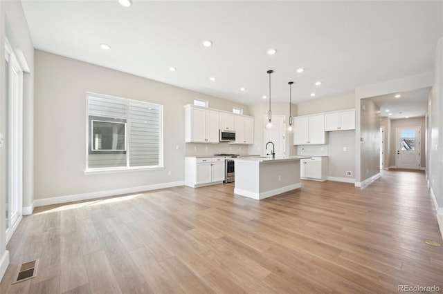 kitchen with a kitchen island with sink, hanging light fixtures, white cabinetry, and stainless steel appliances