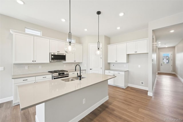 kitchen with appliances with stainless steel finishes, decorative light fixtures, an island with sink, sink, and white cabinets