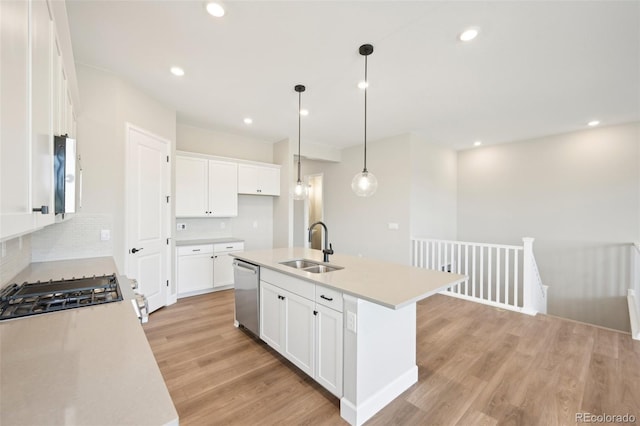 kitchen with decorative light fixtures, white cabinetry, sink, stainless steel dishwasher, and a center island with sink