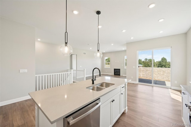 kitchen with pendant lighting, white cabinetry, sink, stainless steel dishwasher, and a center island with sink