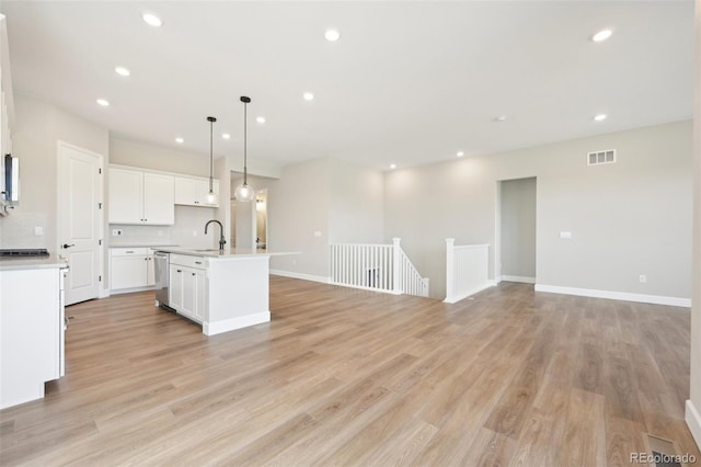 kitchen with pendant lighting, dishwasher, sink, white cabinets, and a kitchen island with sink