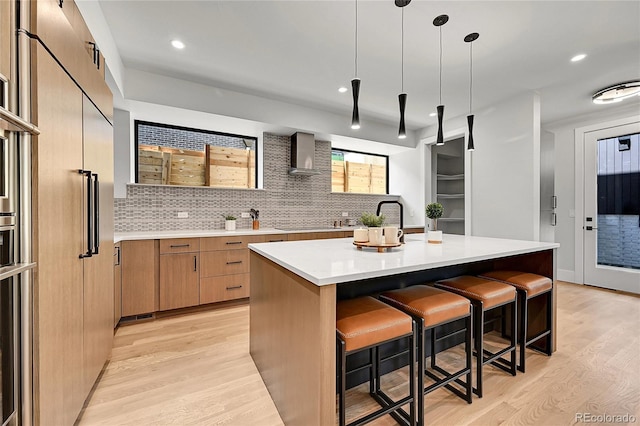 1029 9th St, Boulder, CO 80302 - kitchen featuring modern cabinets, light wood finished floors, wall chimney range hood, a breakfast bar area, and light countertops