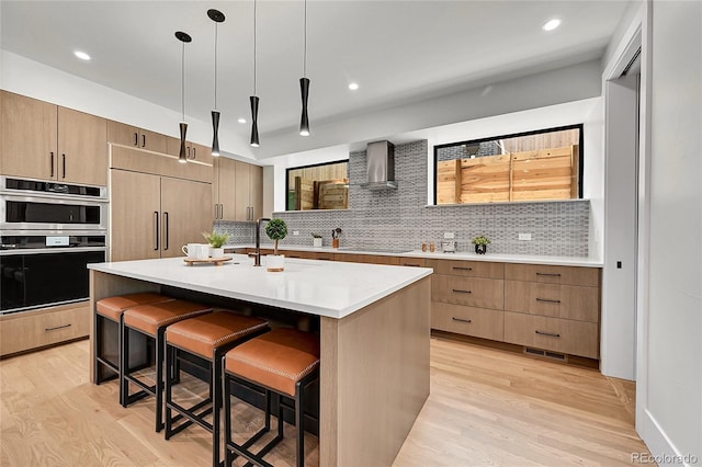 1029 9th St, Boulder, CO 80302 - kitchen featuring wall chimney range hood, a breakfast bar, light wood-style floors, decorative backsplash, and decorative light fixtures