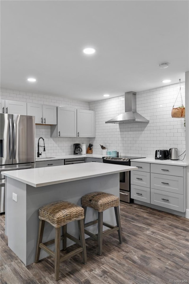 8060 Stuart Pl, Westminster, CO 80031 - kitchen with wall chimney range hood, stainless steel appliances, a kitchen bar, backsplash, and light countertops