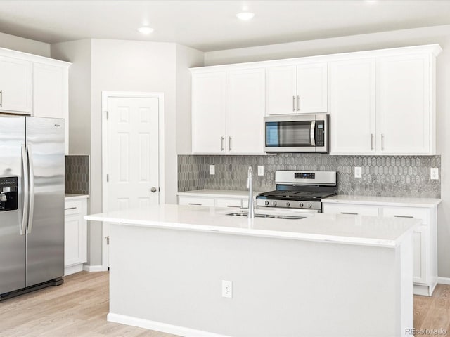 kitchen featuring appliances with stainless steel finishes, backsplash, light wood finished floors, and an island with sink