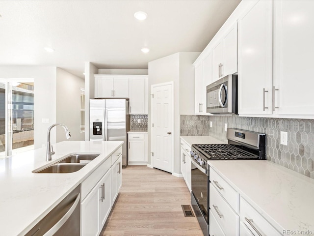 kitchen featuring light wood-type flooring, recessed lighting, white cabinets, a sink, and appliances with stainless steel finishes