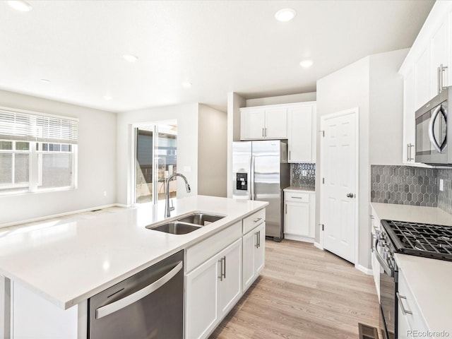 kitchen featuring backsplash, appliances with stainless steel finishes, a sink, light countertops, and light wood finished floors