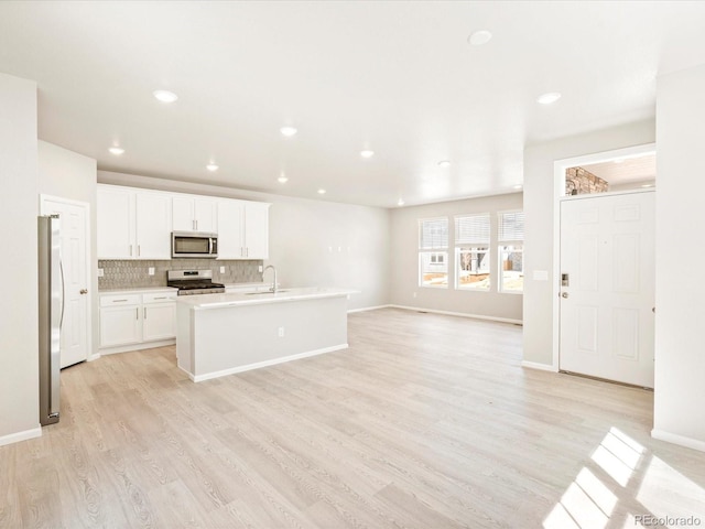 kitchen featuring tasteful backsplash, light wood-type flooring, a sink, open floor plan, and stainless steel appliances