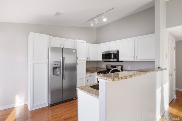 3857 Mossy Rock Dr Unit 201, Highlands Ranch, CO 80126 - kitchen with stainless steel appliances, track lighting, light wood-style floors, a peninsula, and high vaulted ceiling