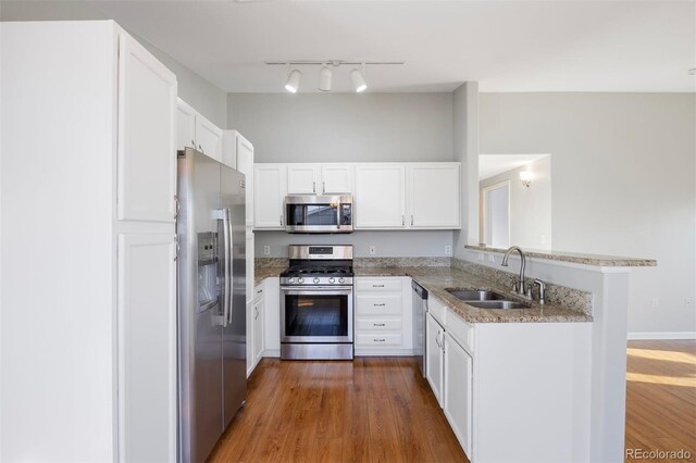 3857 Mossy Rock Dr Unit 201, Highlands Ranch, CO 80126 - kitchen with stainless steel appliances, light stone counters, white cabinetry, a peninsula, and wood finished floors