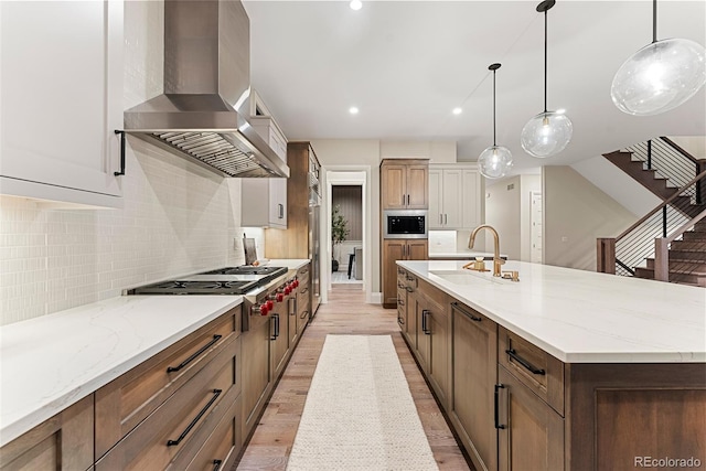 kitchen with wall chimney exhaust hood, sink, hanging light fixtures, a large island with sink, and appliances with stainless steel finishes